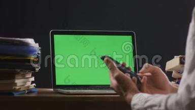人类正在使用智能手机，他的笔记本电脑上有一个绿色屏幕或一个色度在他的桌面上。 商人在这里工作